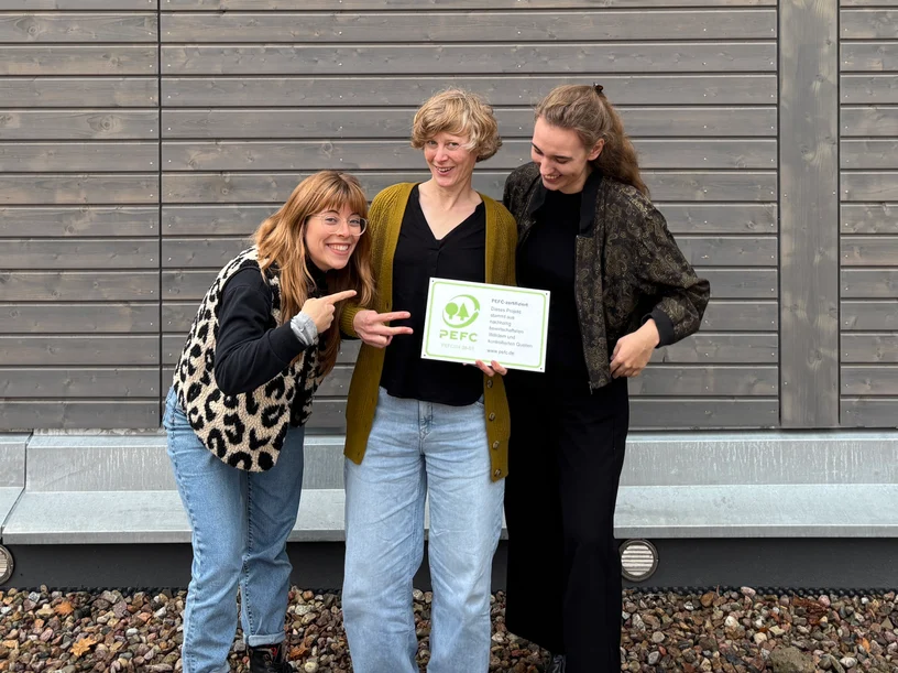 Anna (Nachhaltigkeitsmanagerin), Neele (Praktikantin im Bereich Nachhaltigkeit) und Annika (Managerin Marketing + Kommunikation) präsentieren das PEFC-Zertifikat stolz